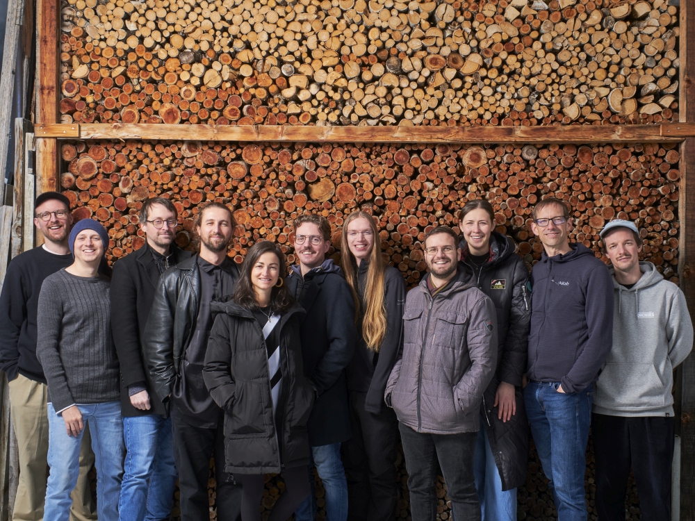 Die 11-köpfige Band vor einer Wand aus aufgeschichtetem Holz