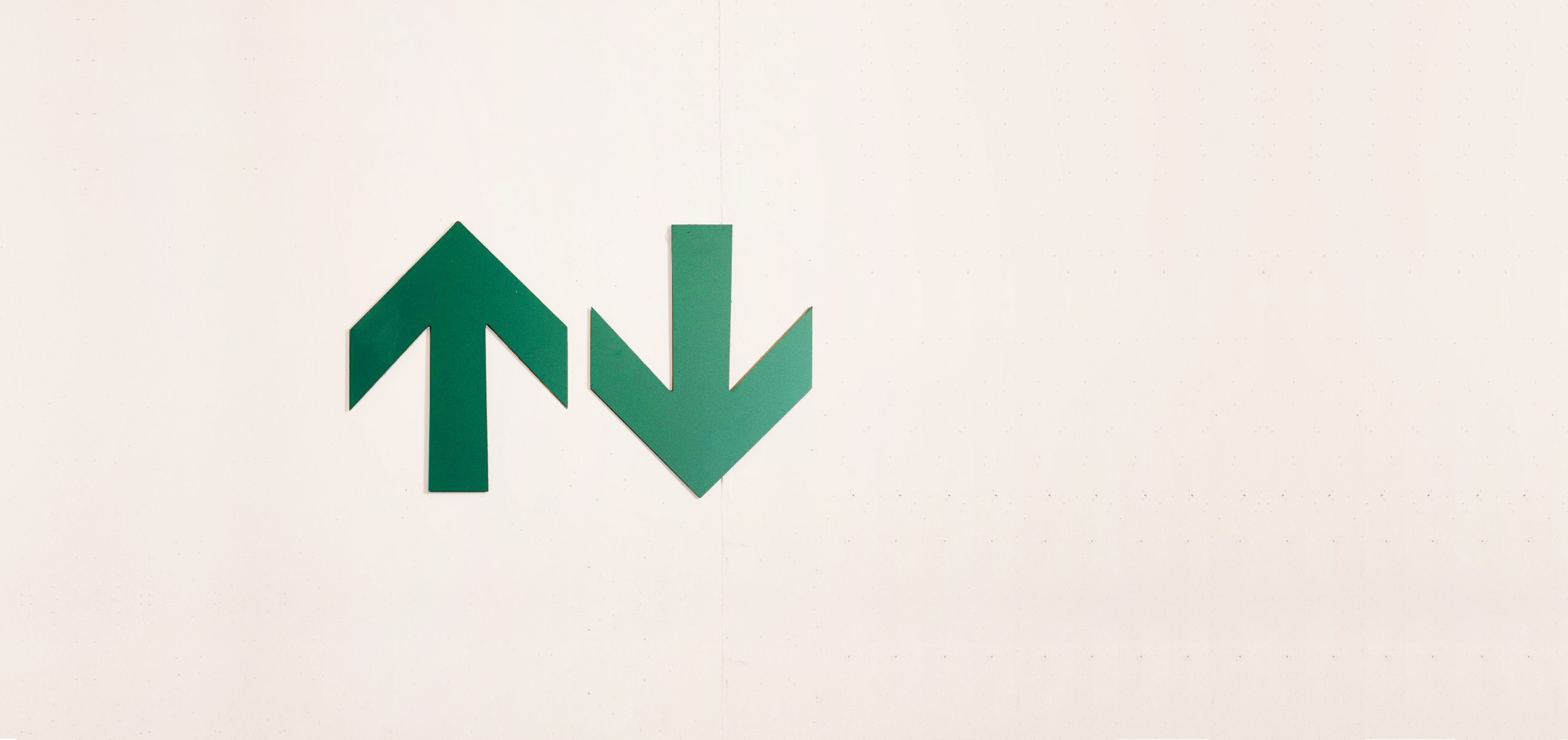 Two green arrows on a concrete wall point up and down respectively