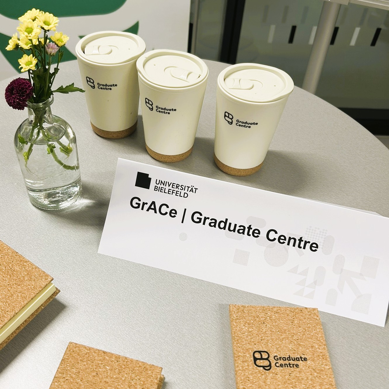 Schräge Überansicht des Tischstandes vom GrACe (Graduate Centre) mit Give-aways wie Kaffeebechern.
