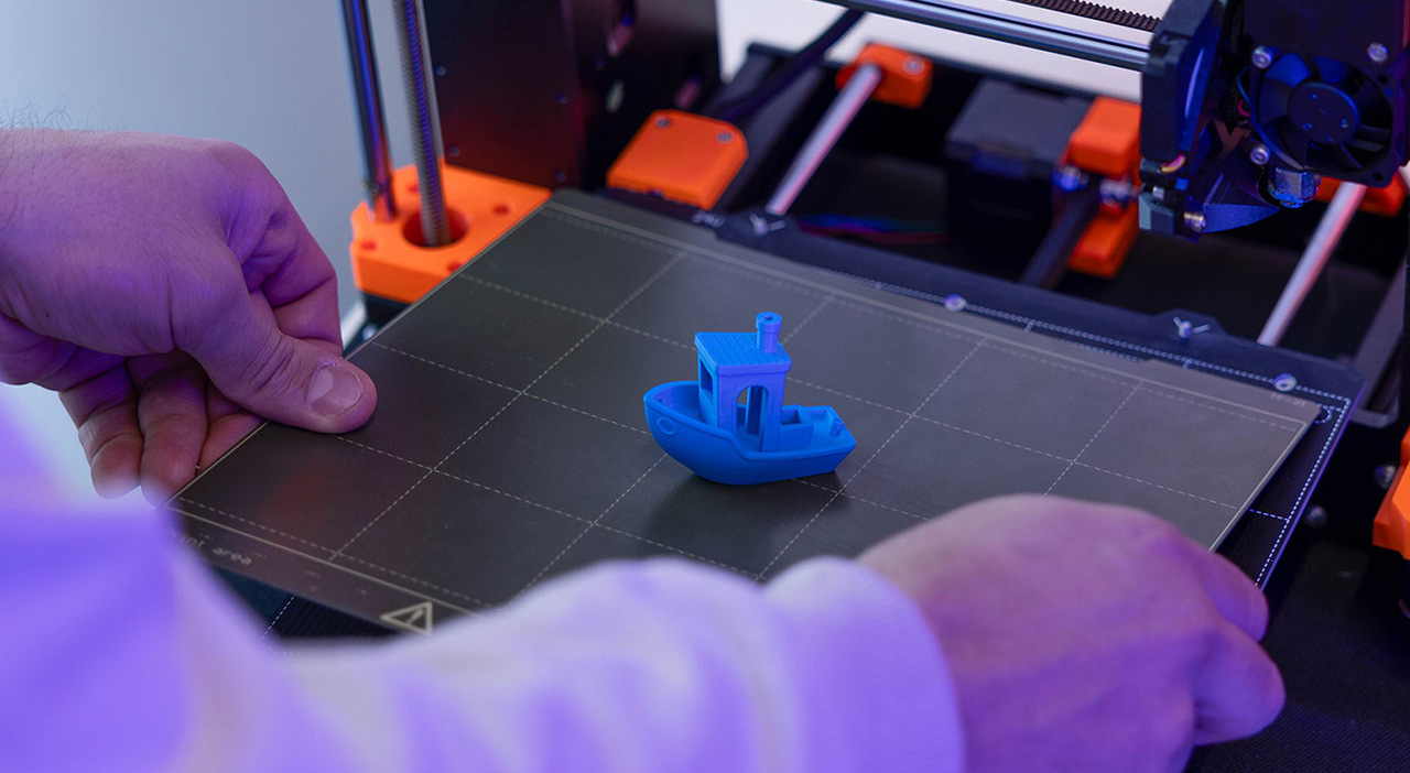 Gedrucktes Boot auf einem 3D-Drucker. Zwei Hände heben die Trägermatte hoch.