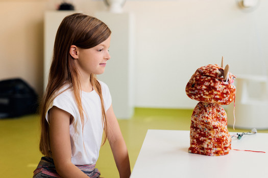Ein junges Mädchen sitzt an einem Tisch. Vor ihr steht ein Roboter.