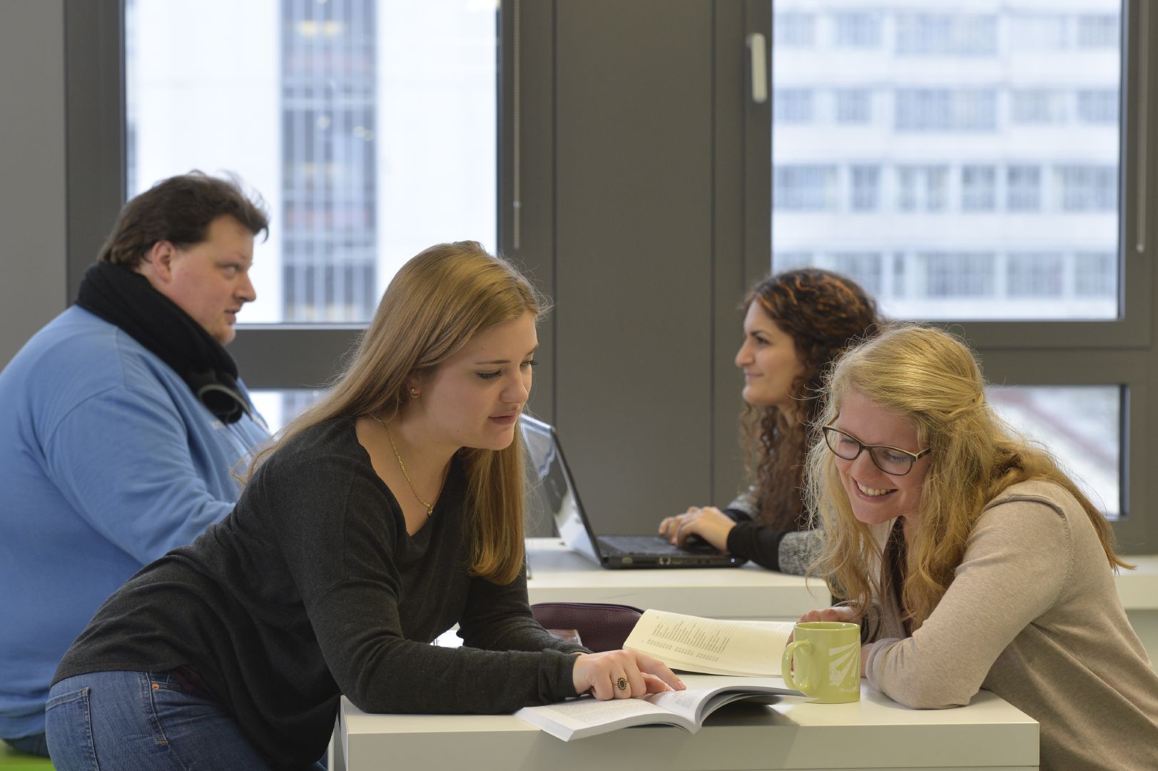 Zwei Studentinnen sitzen gemeinsam an einem Tisch und schauen in ein Buch