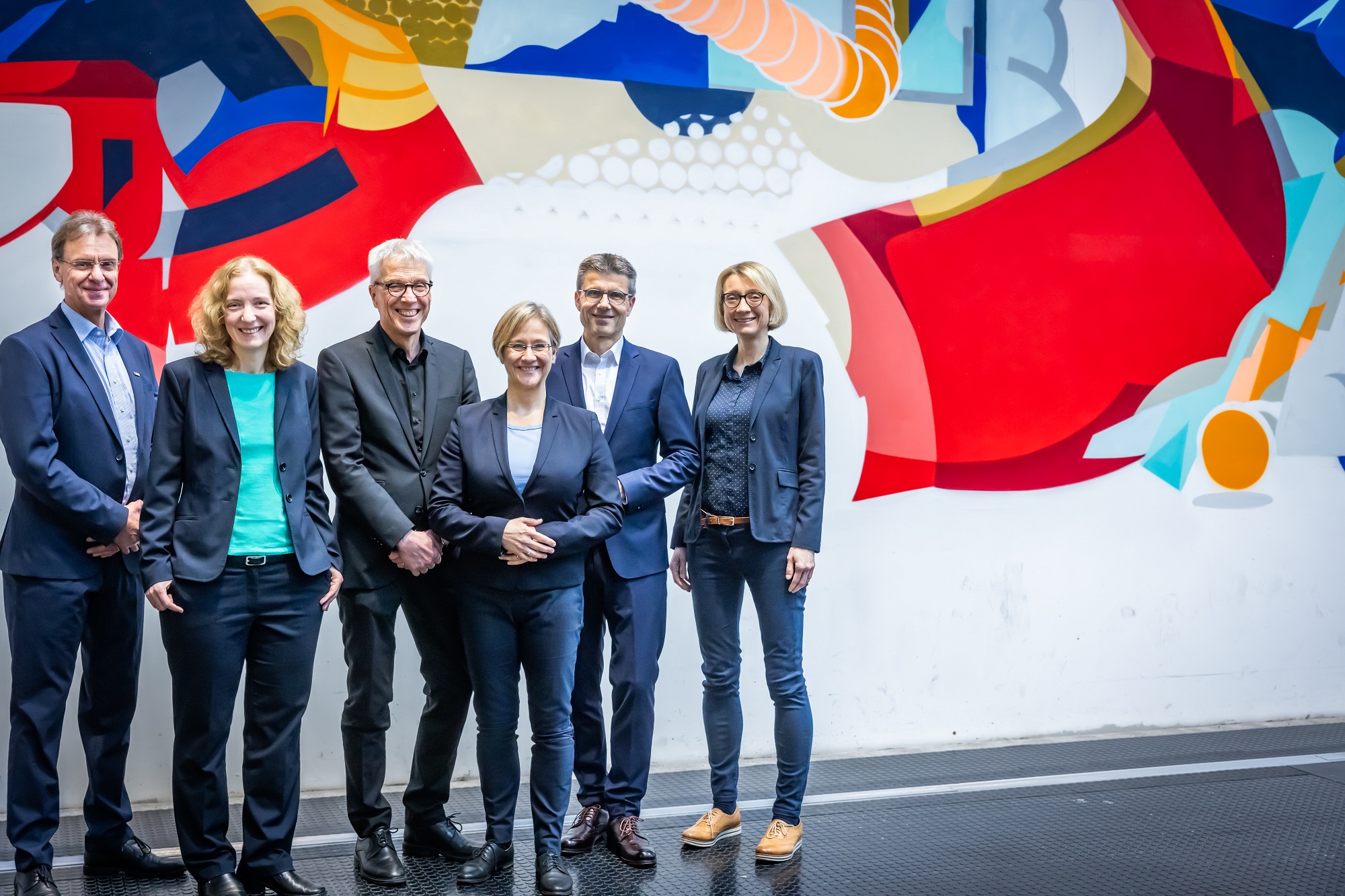 The six members of the rectorate stand in front of the graffiti wall in the central university hall.