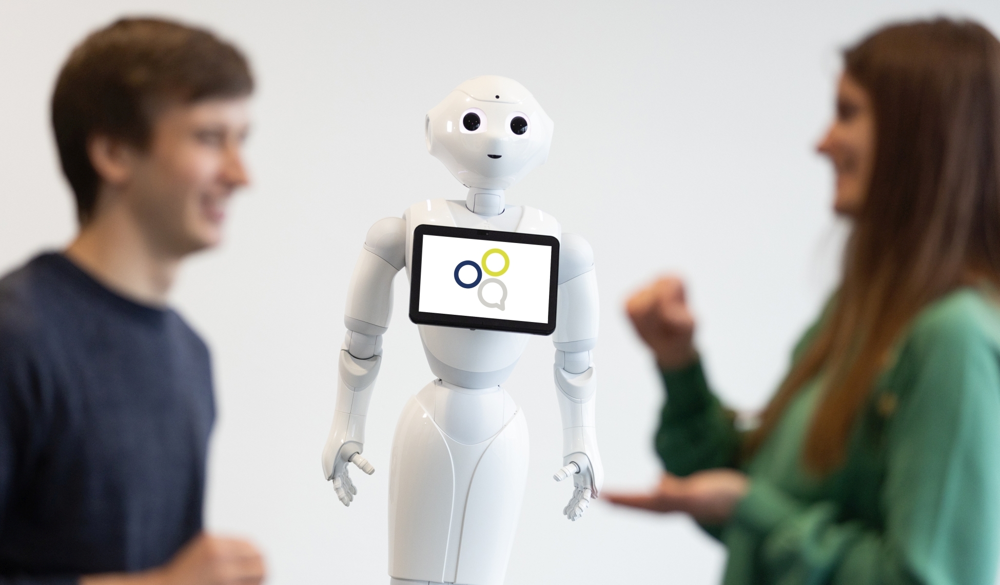 Ein weißer humanoider Roboter, daneben ein Mann und eine Frau im Gespräch.