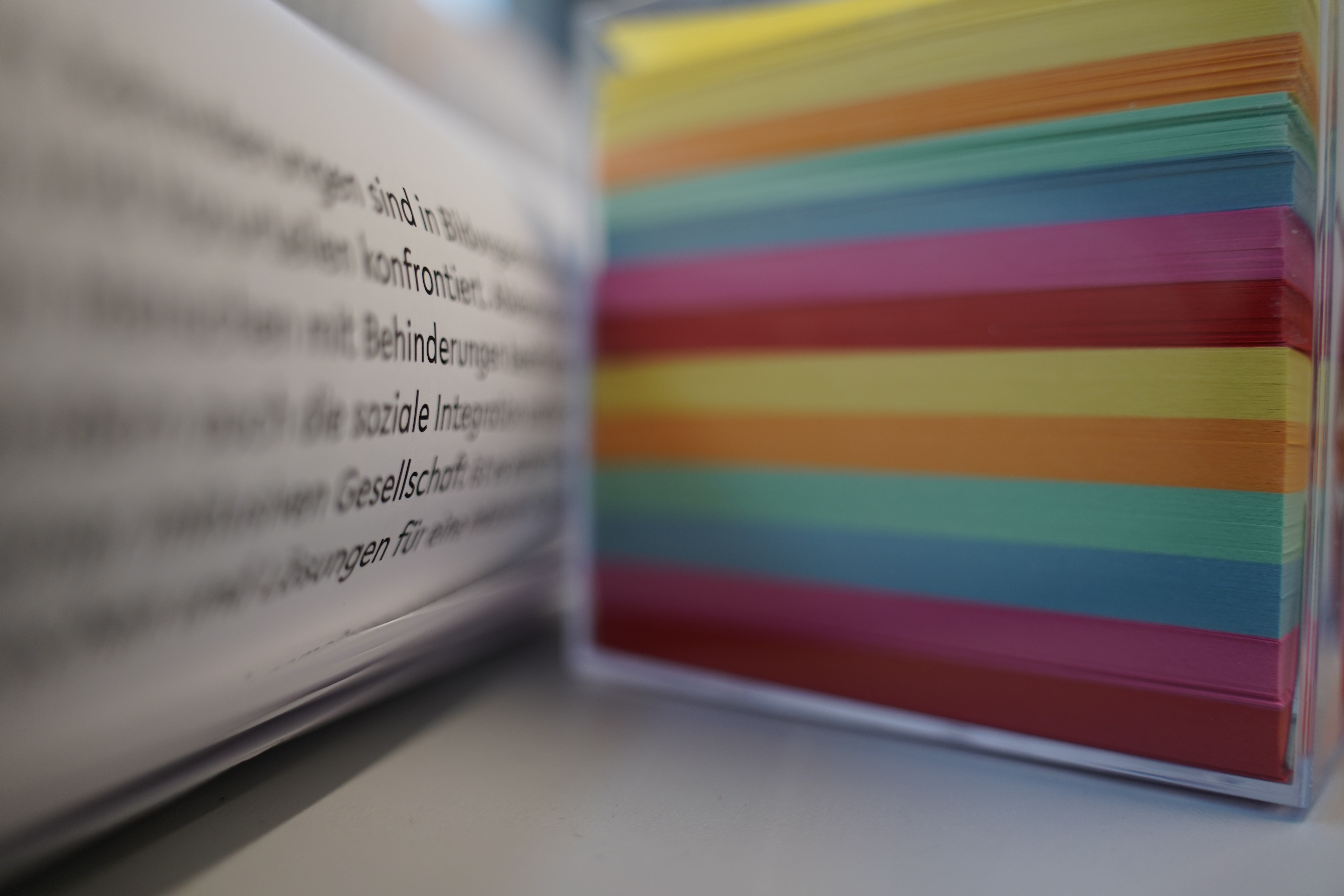 Foto: Auf der linken Seite ist ein ausgedruckter Text, deren Buchstaben verschwommen sind. Aus der rechten Seite ist ein Stapel mit buntem Papier.