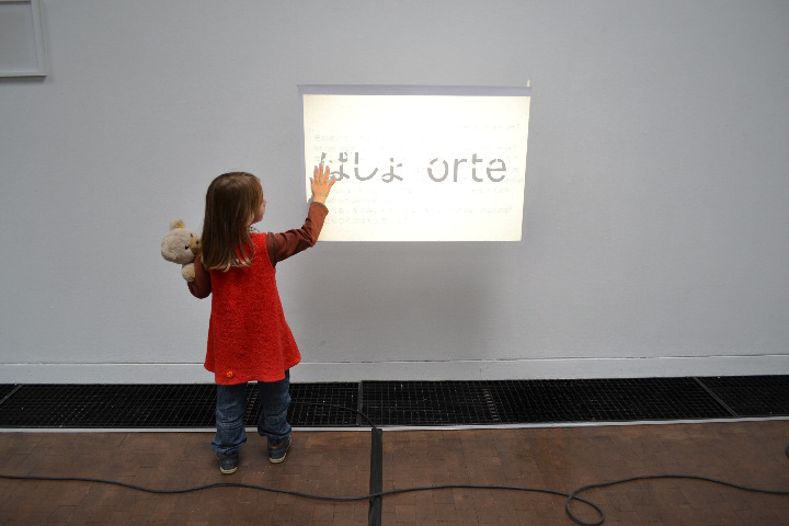 Two children stand in front of a projected image with writing
