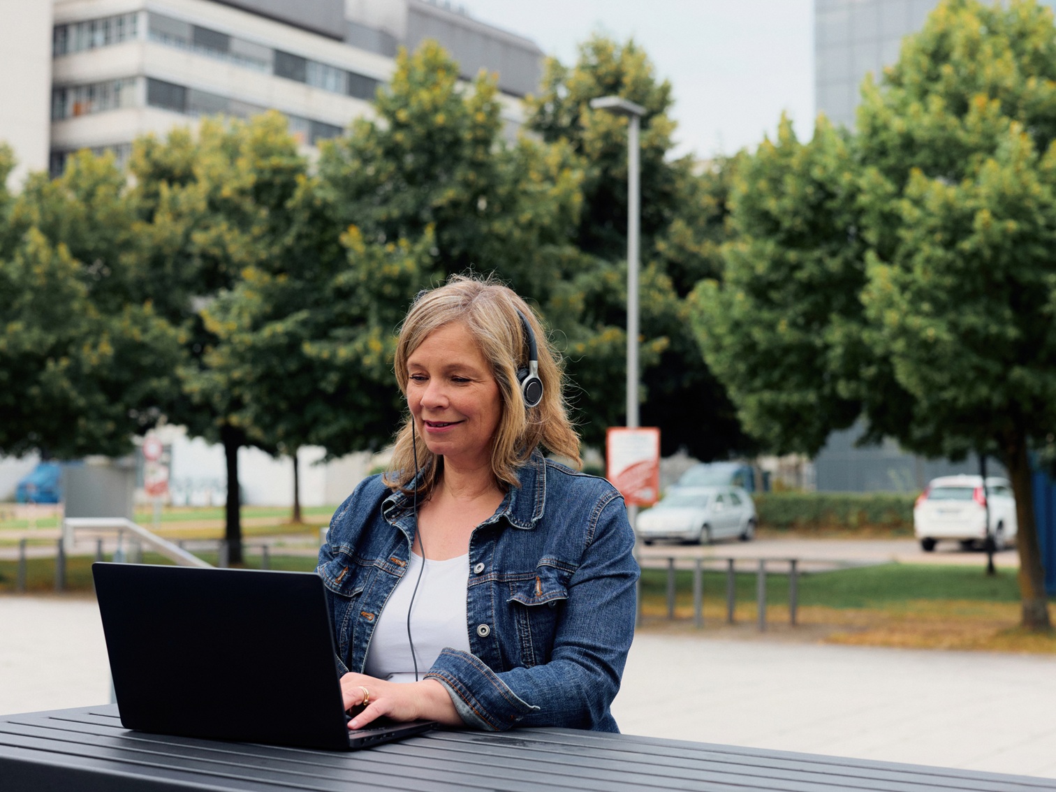 Person sitzt mit Headset draußen am Laptop