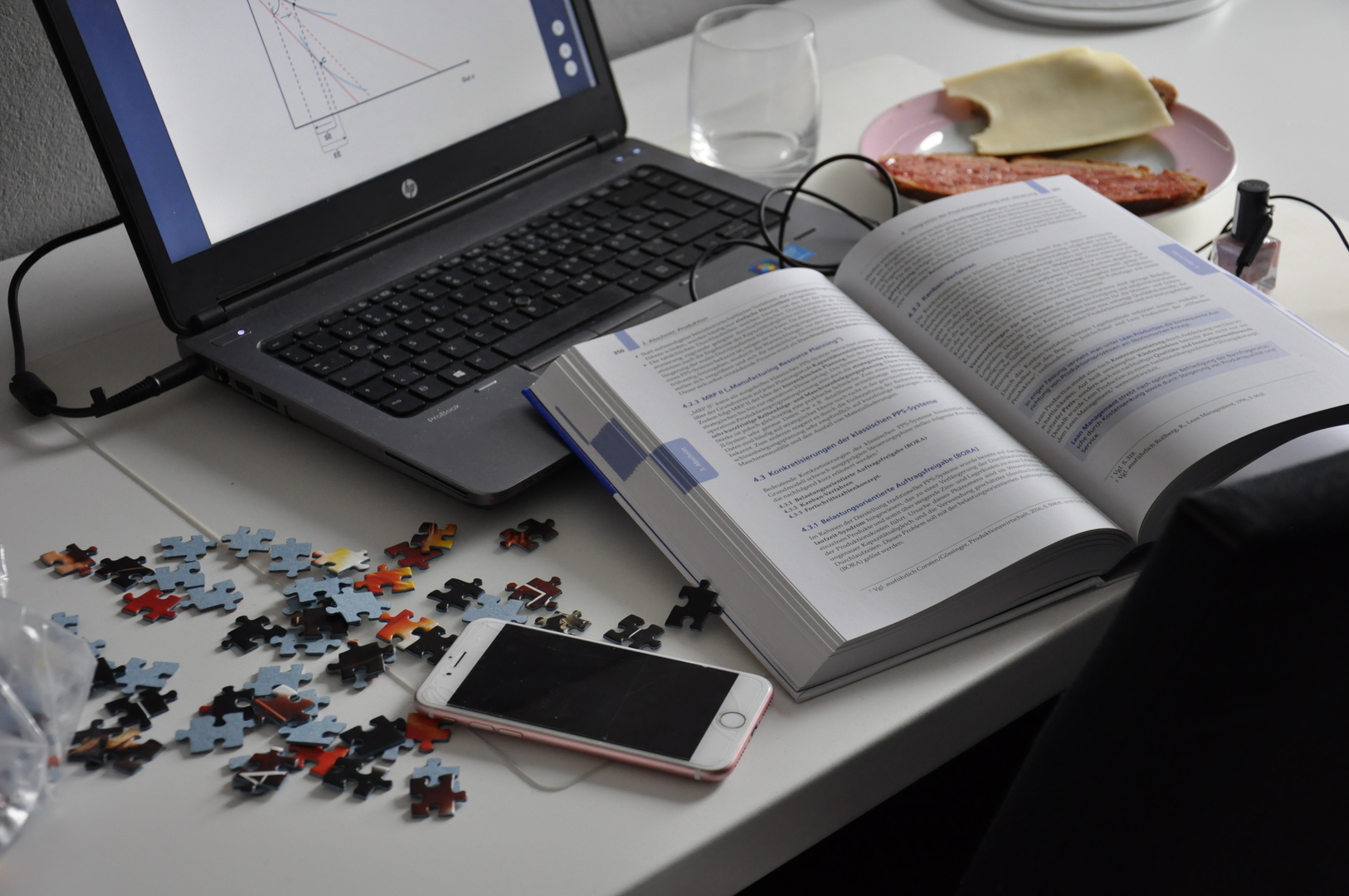 Schreibtisch, auf dem Laptop, Buch, Smartphone und Schreiutensilien durcheinander liegen
