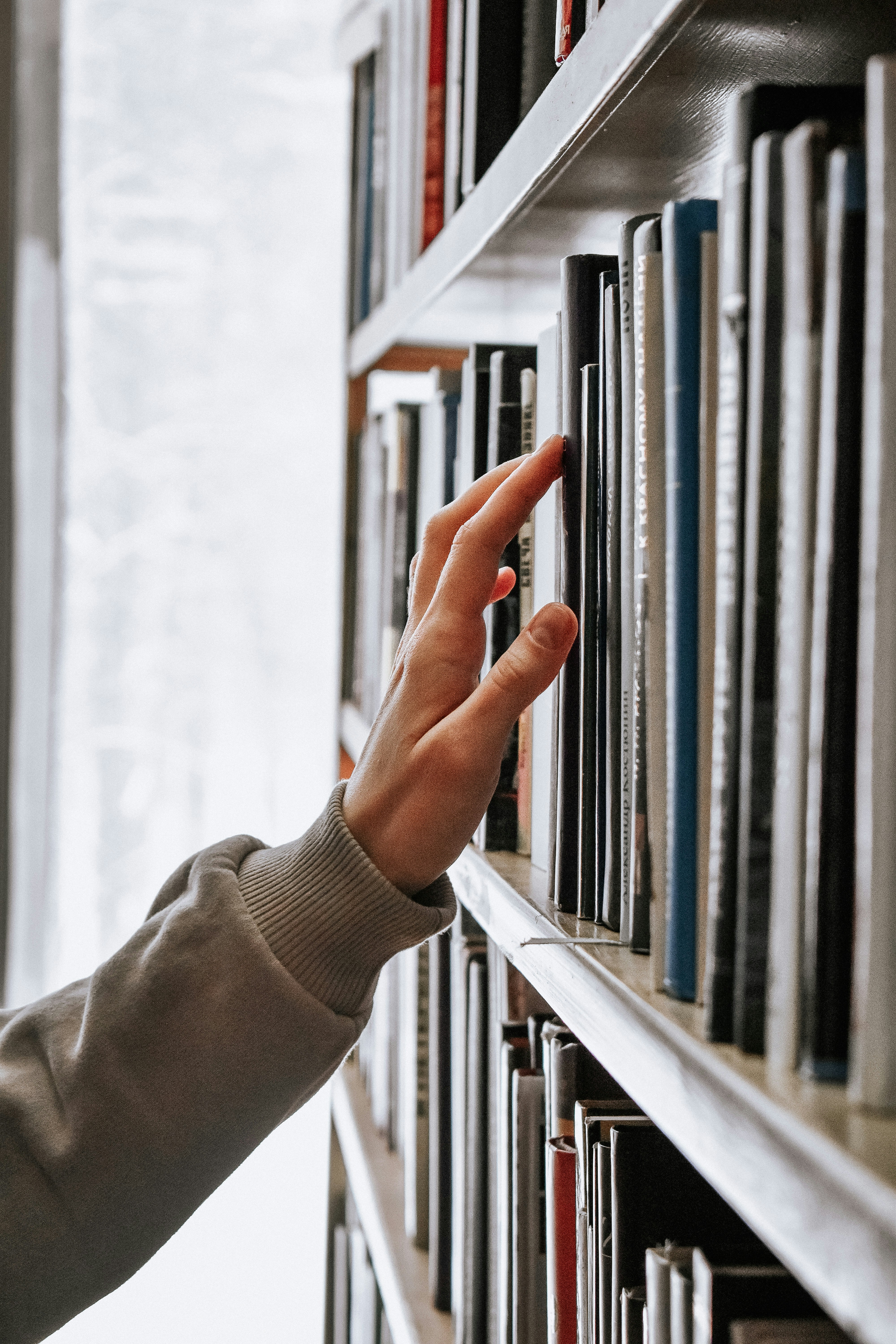 eine Person nimmt mit ihrer Hand ein Buch aus dem Bücherregal einer Bibliothek