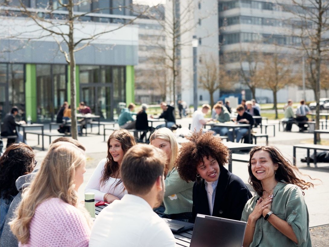 Studierende der Fakultät für Soziologie an der Universität Bielefeld im Gespräch auf dem Campusgelände vor Gebäude X, bei sonnigem Wetter – modernes Universitätsleben in NRW mit Fokus auf Austausch und Gemeinschaft