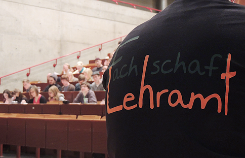 Fünf Fachschaftler*innen vor Erstsemesterstudierenden in einem Hörsaal.
