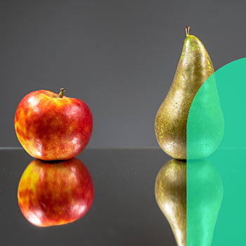 Red apple and green pear side by side on a smooth surface