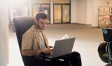 Ein Mann arbeitet im Sessel mit dem Laptop