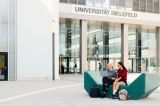 Two students sitting in front of the main entrance to Bielefeld University's main building