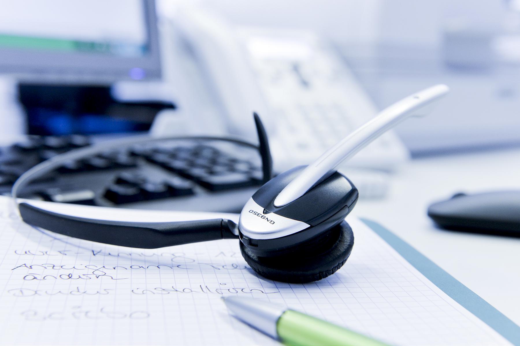 Desk with headset, keyboard, mouse, pen and notes