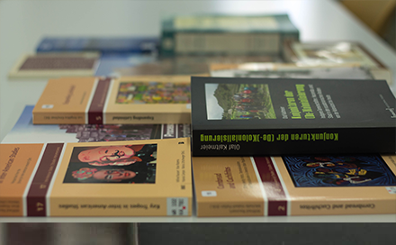 Kachel Bücher in Auswahl mit Link zur Übersichtsseite einer Buchauswahl. Das Bild zeigt mehrere auf dem Tisch liegende Bücher