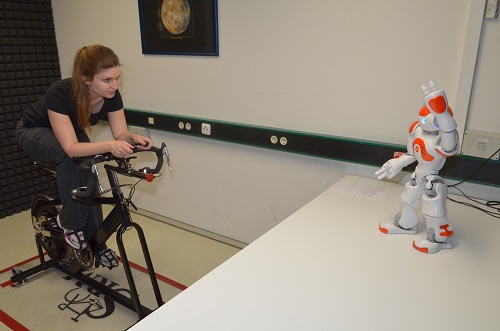 Woman indoor cycling with robot Nao on table in front