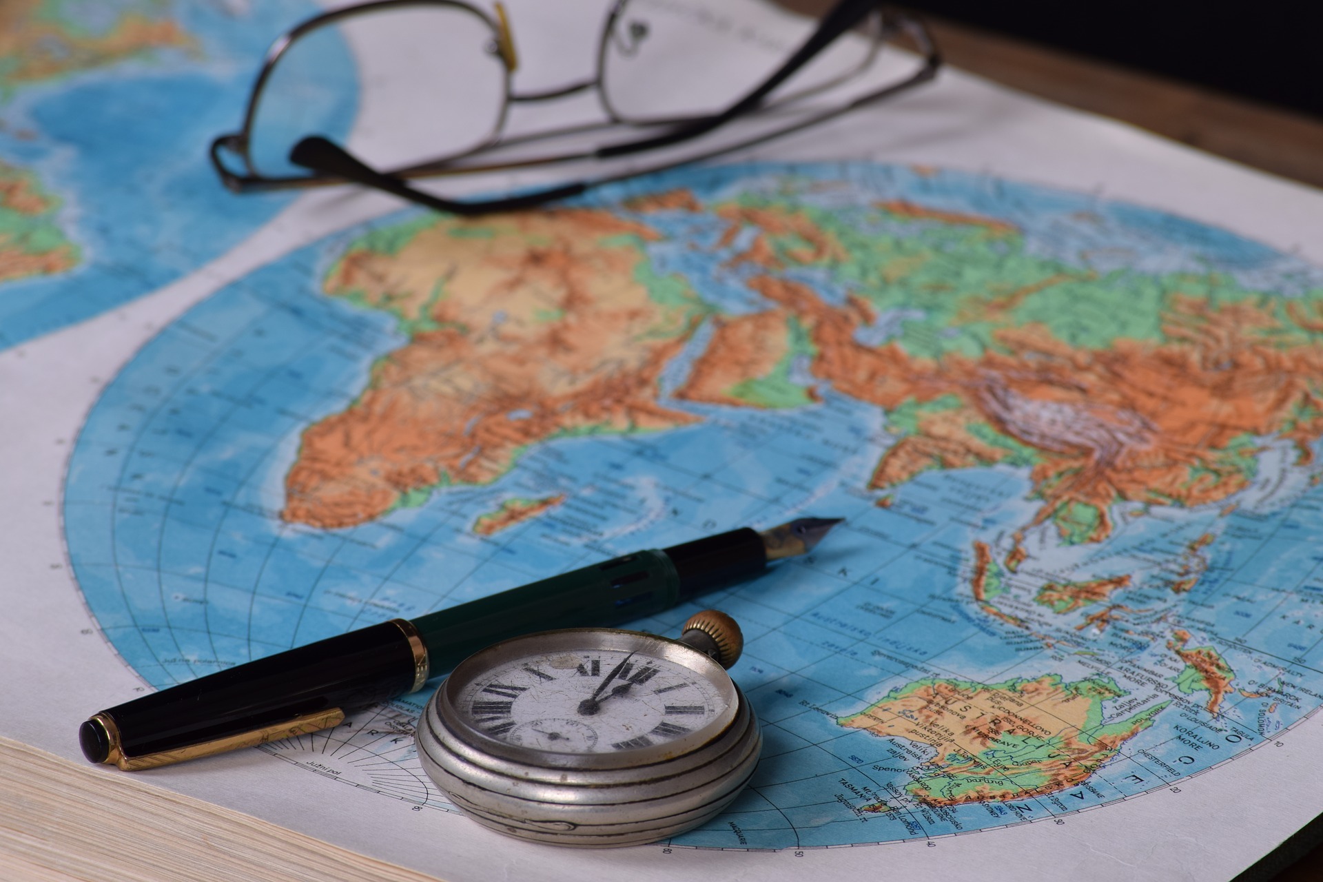 Ein Kugelschreiber, eine Brille und eine Taschenuhr auf einer Weltkarte.