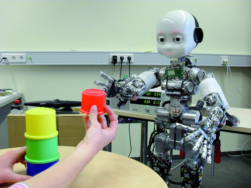 A person offers a humanoid robot a red stacking cup to grasp