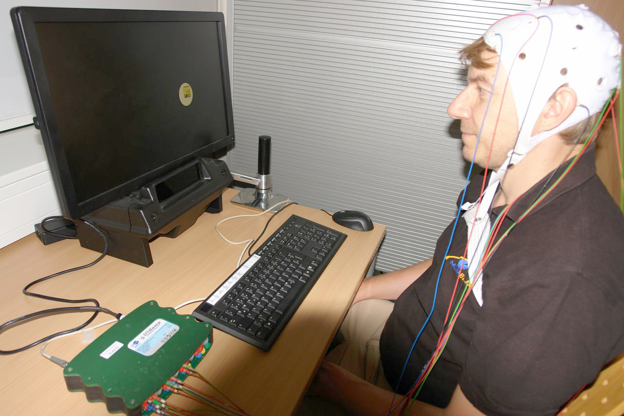 A person wearing an EEG cap in front of a screen and a keyboard