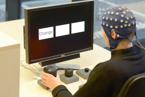A person wearing an EEG cap sitting in front of a table with a screen and touch buttons