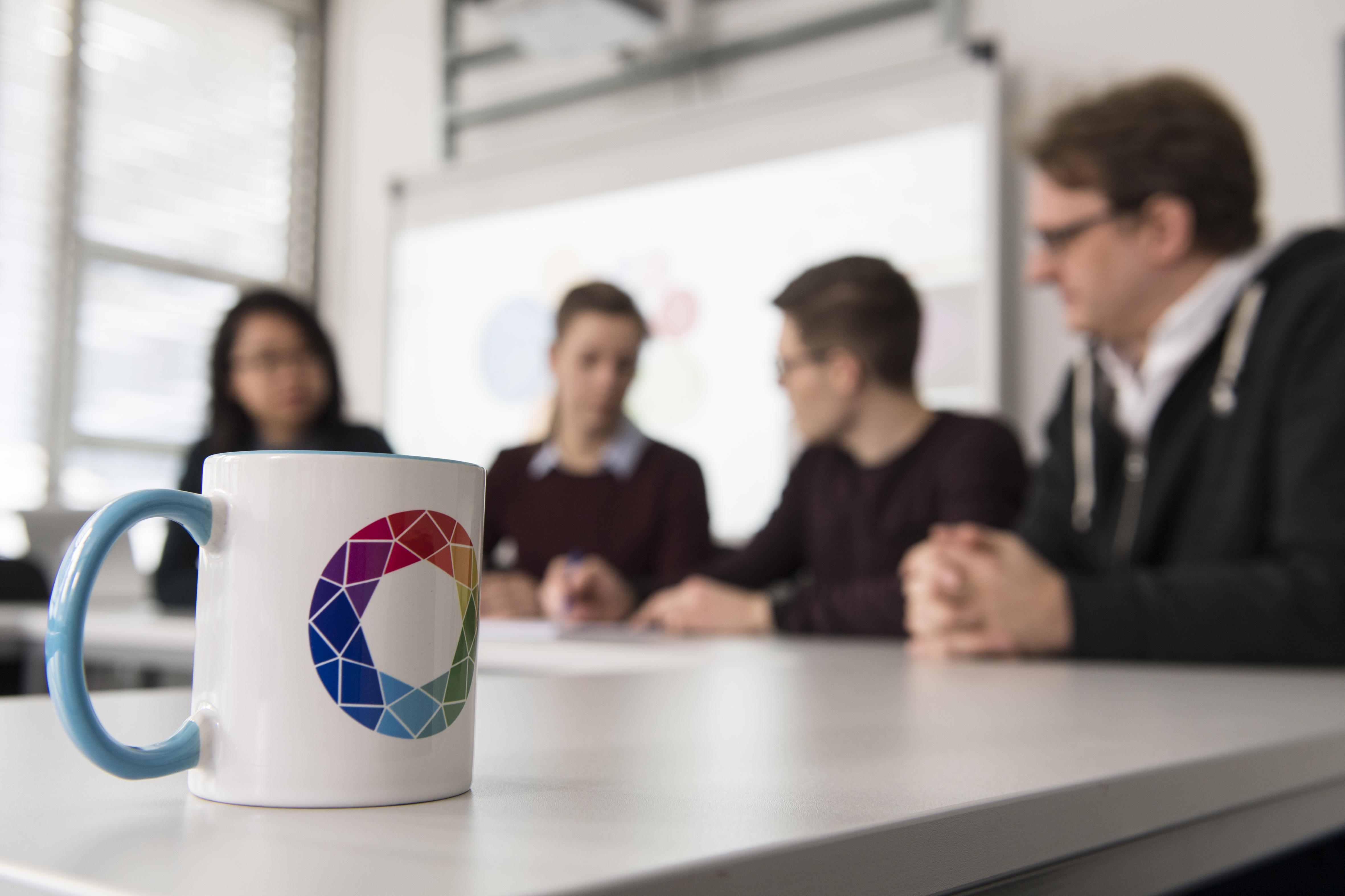 Vier Forscher*innen im Gespräch sitzen an Tisch, Tasse im Vordergrund