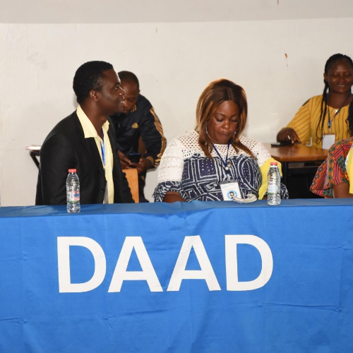 People sitting behind a table with a blue banner with DAAD (German Academic Exchange Service) lettering spread over it.