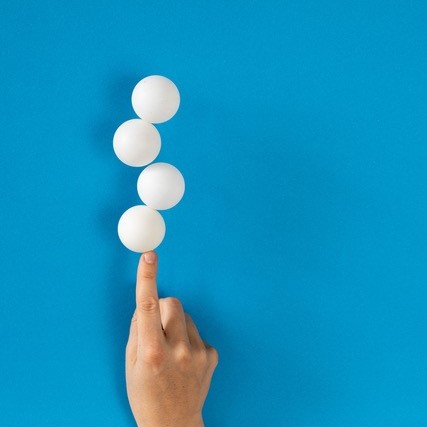 A hand balances table tennis balls against a blue background
