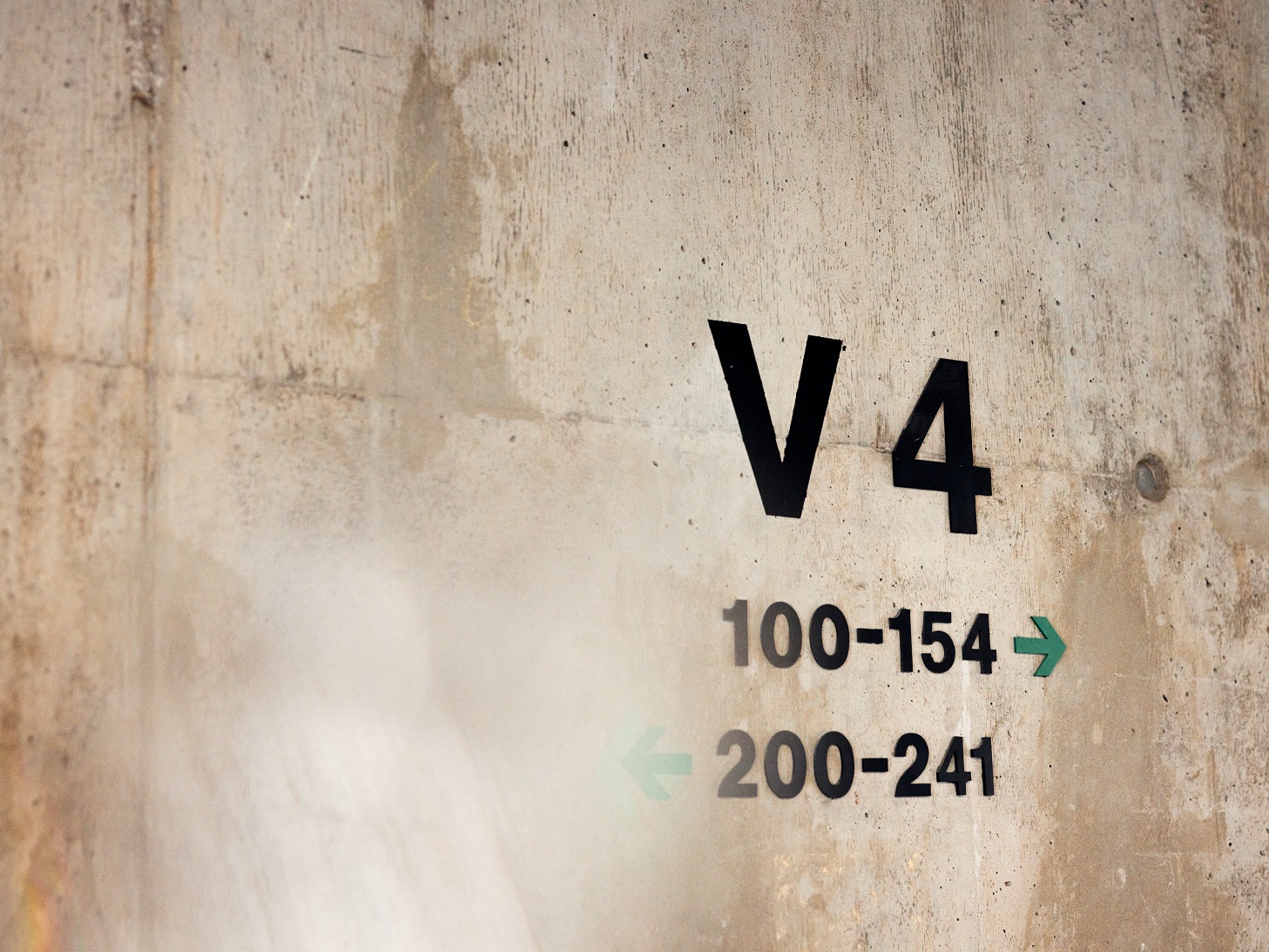Schriftzug "V4" und Pfeile mit Raumnummern auf einer Betonwand