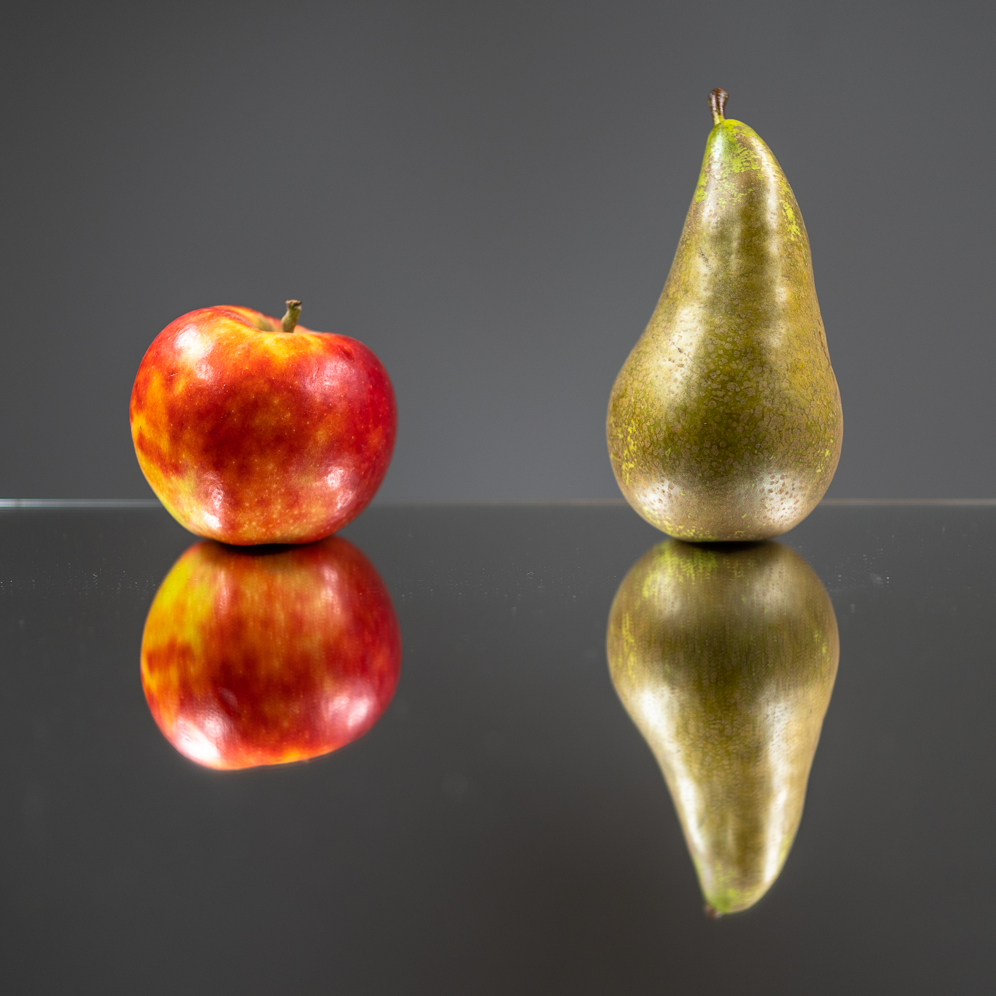 Ein Apfel und eine Birne liegen auf einer glänzenden Oberfläche und spiegeln sich darin.