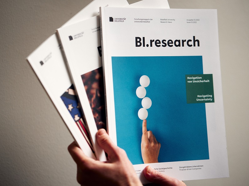 Hand holds three issues of the research magazine