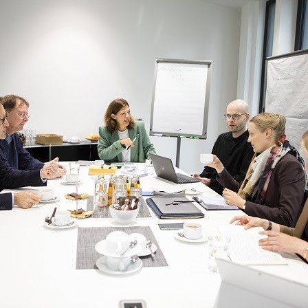 Mindestens sechs Personen sitzen um einen Konferenztisch herum