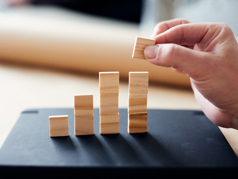 Hand adds new building block to a row of stacked wooden building blocks