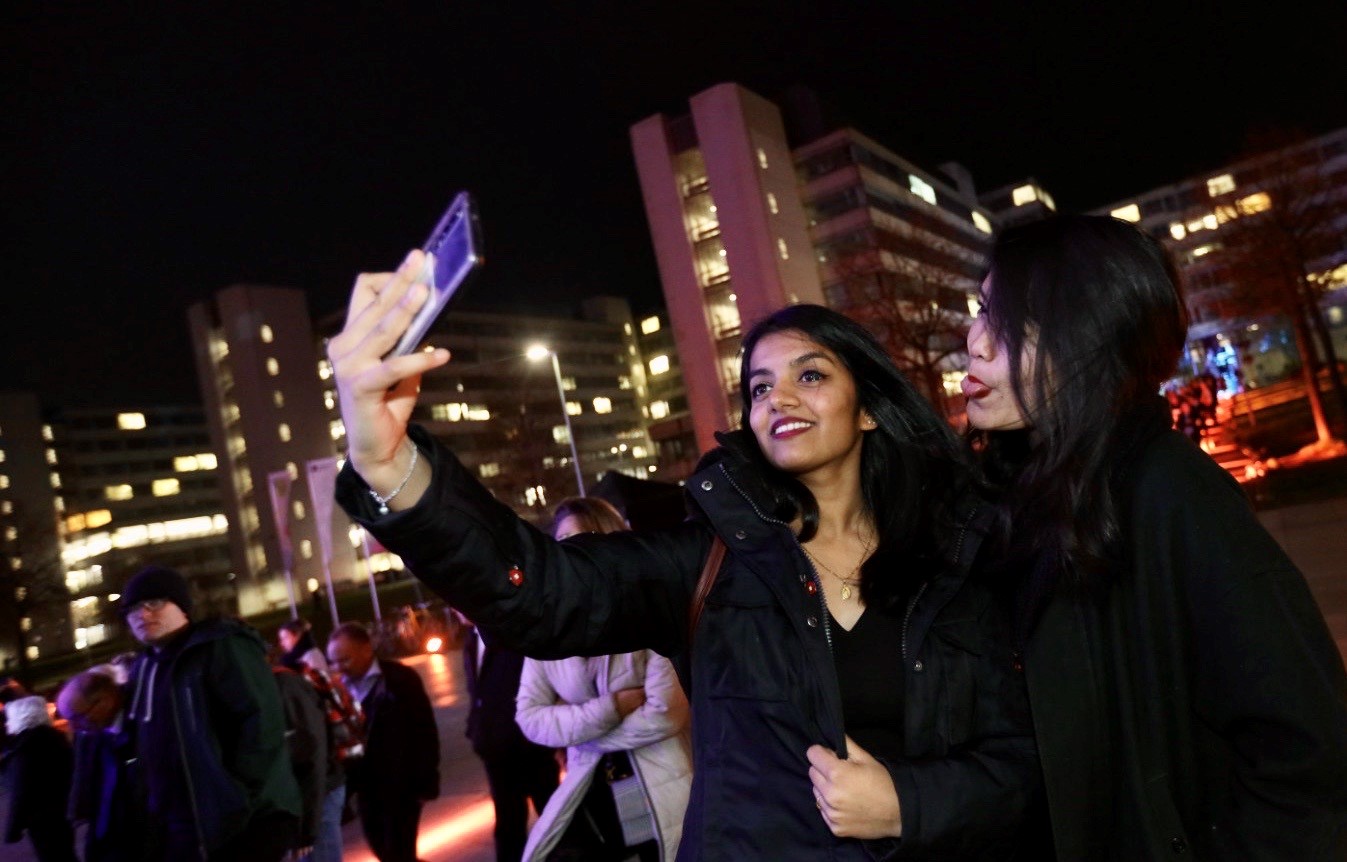 Zwei Gäste machen ein Selfie, im Hintergrund ist das Hauptgebäude am Abend