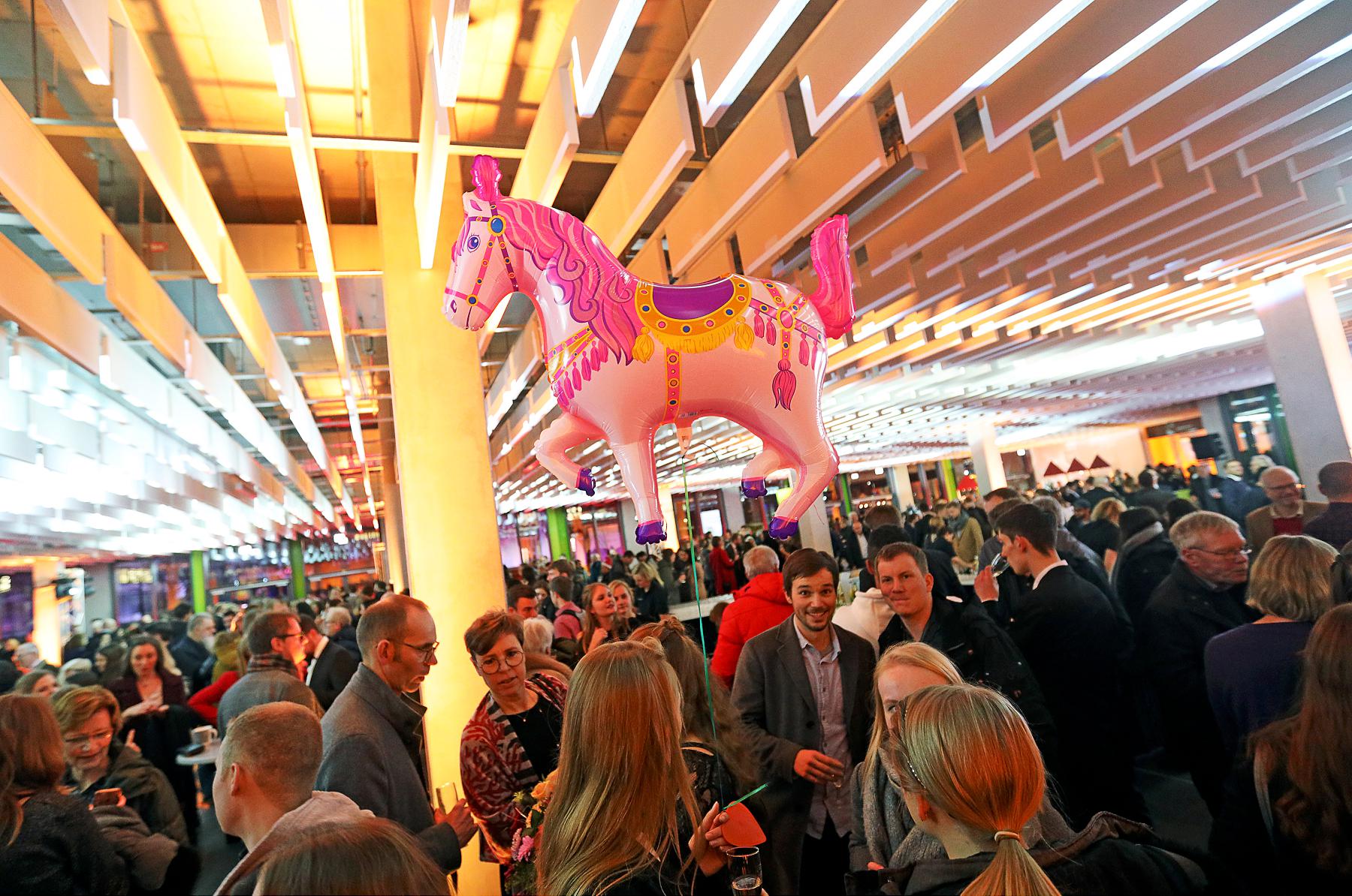 Viele Gäste im X-Gebäude und in der Mitte schwebt ein Luftballon in Form eines Pferdes