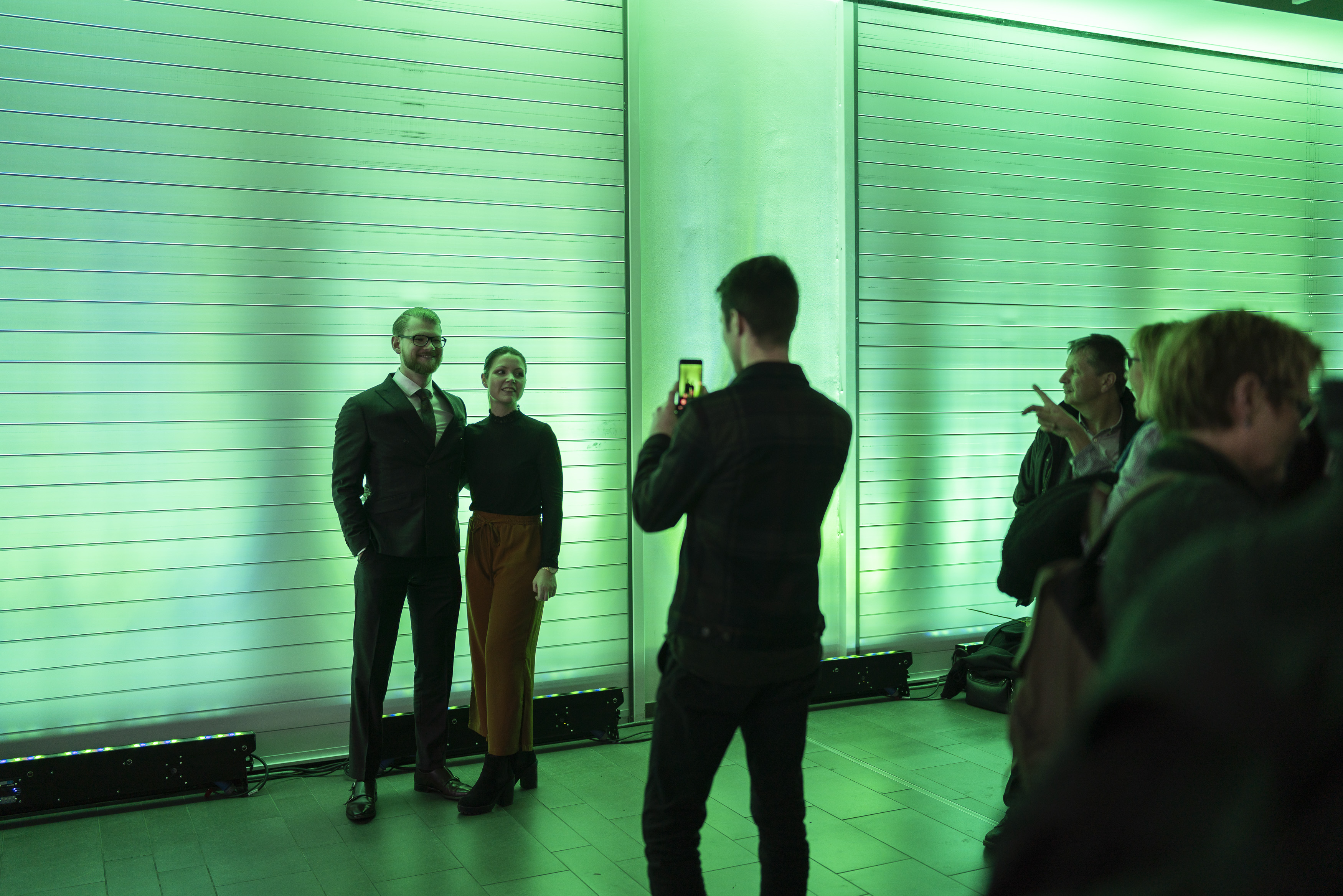 Zwei Gäste werden vor einer grün angeleuchteten Wand fotografiert