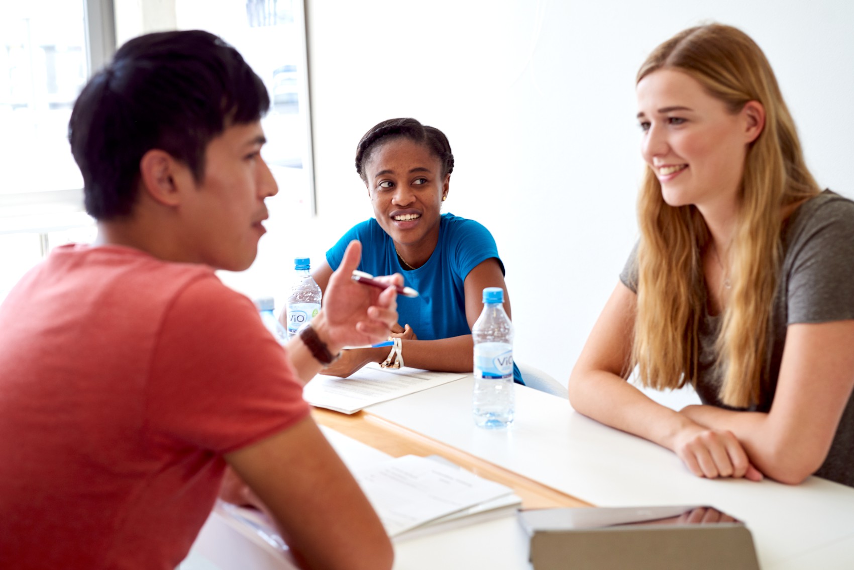 Zwei Studentinnen und ein Student sitzen an einem Tisch und unterhalten sich