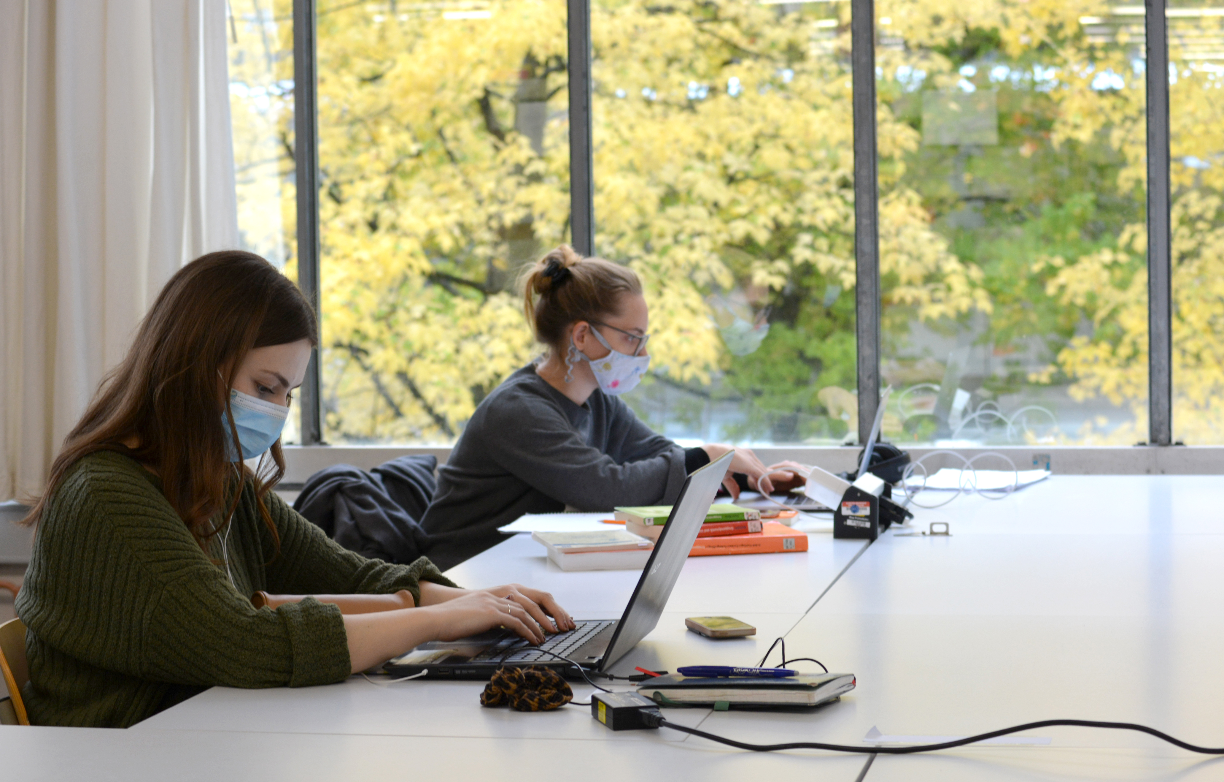 Zwei Studentinnen mit Alltagsmaske an Arbeitsplätzen der Bibliothek