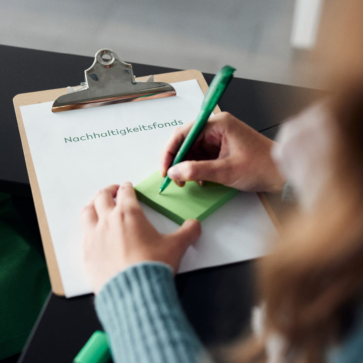 Blick über die Schulter einer Person, die sich auf einem Klemmbret mit der Beschriftung Nachhaltigkeitsfonds Notizen macht