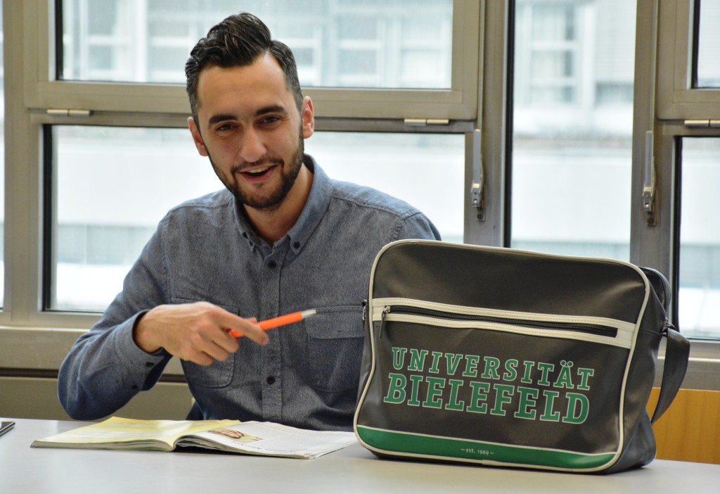 Student sitzt in einem Seminarraum, auf dem Tisch liegt eine Tasche der Universität Bielefeld