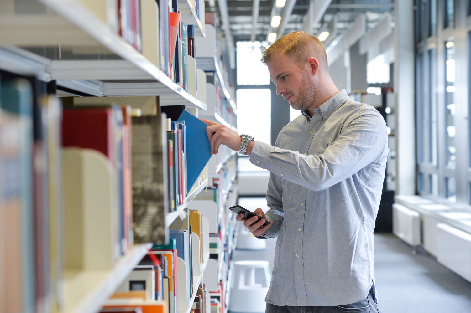 Person at the bookshelf with smartphone in hand
