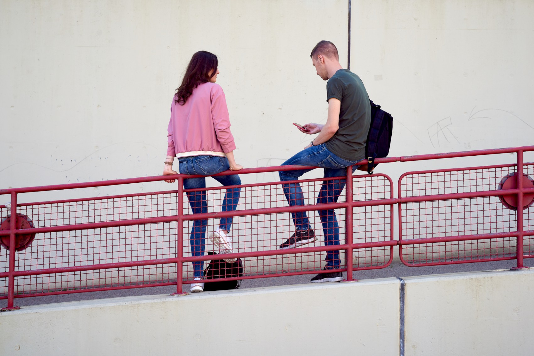 Two students sit on the red railing at the ramp