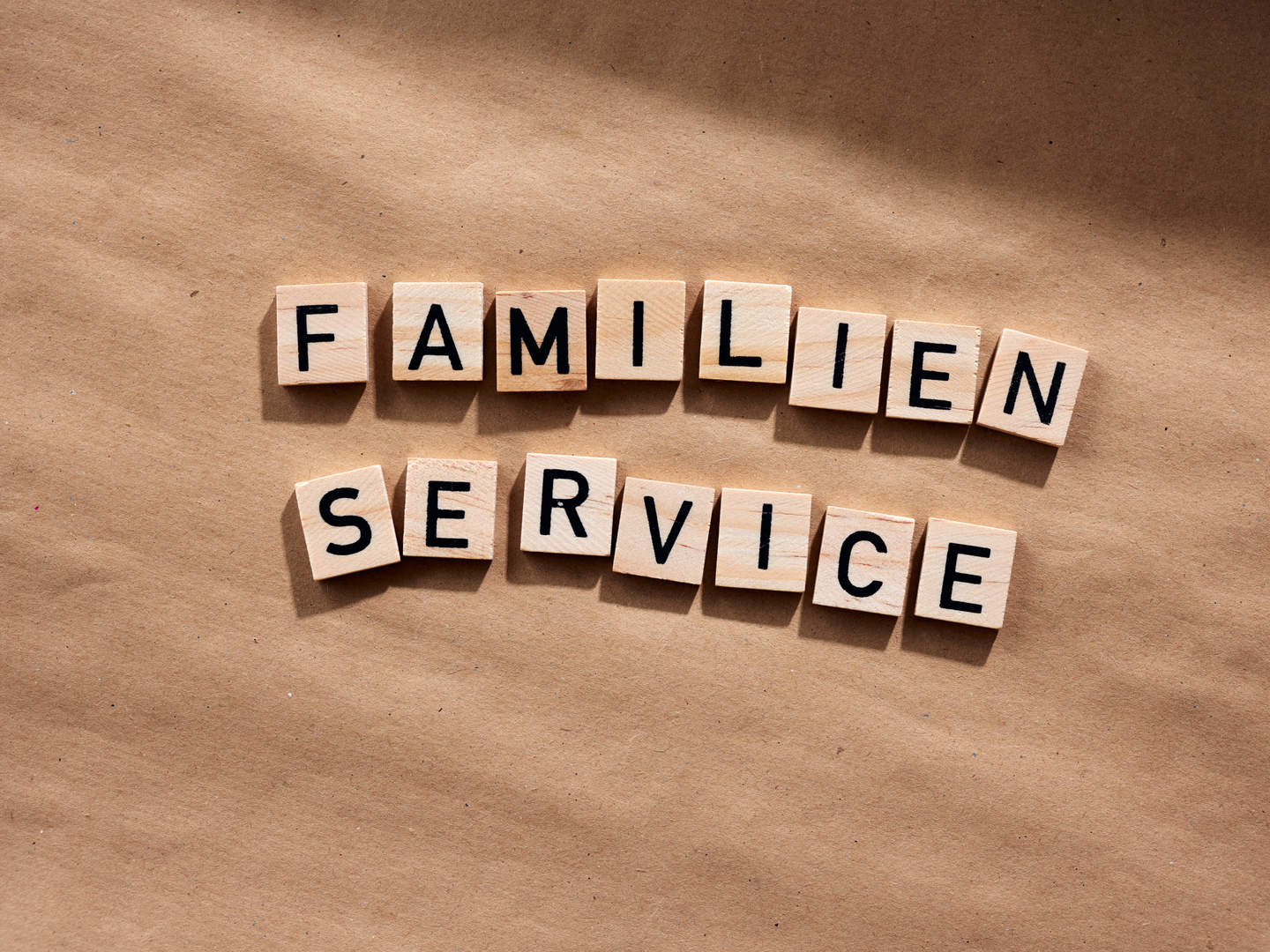 Holztäfelchen mit Buchstaben liegen auf einem Tisch und zeigen den Schriftzug "Familien Service"
