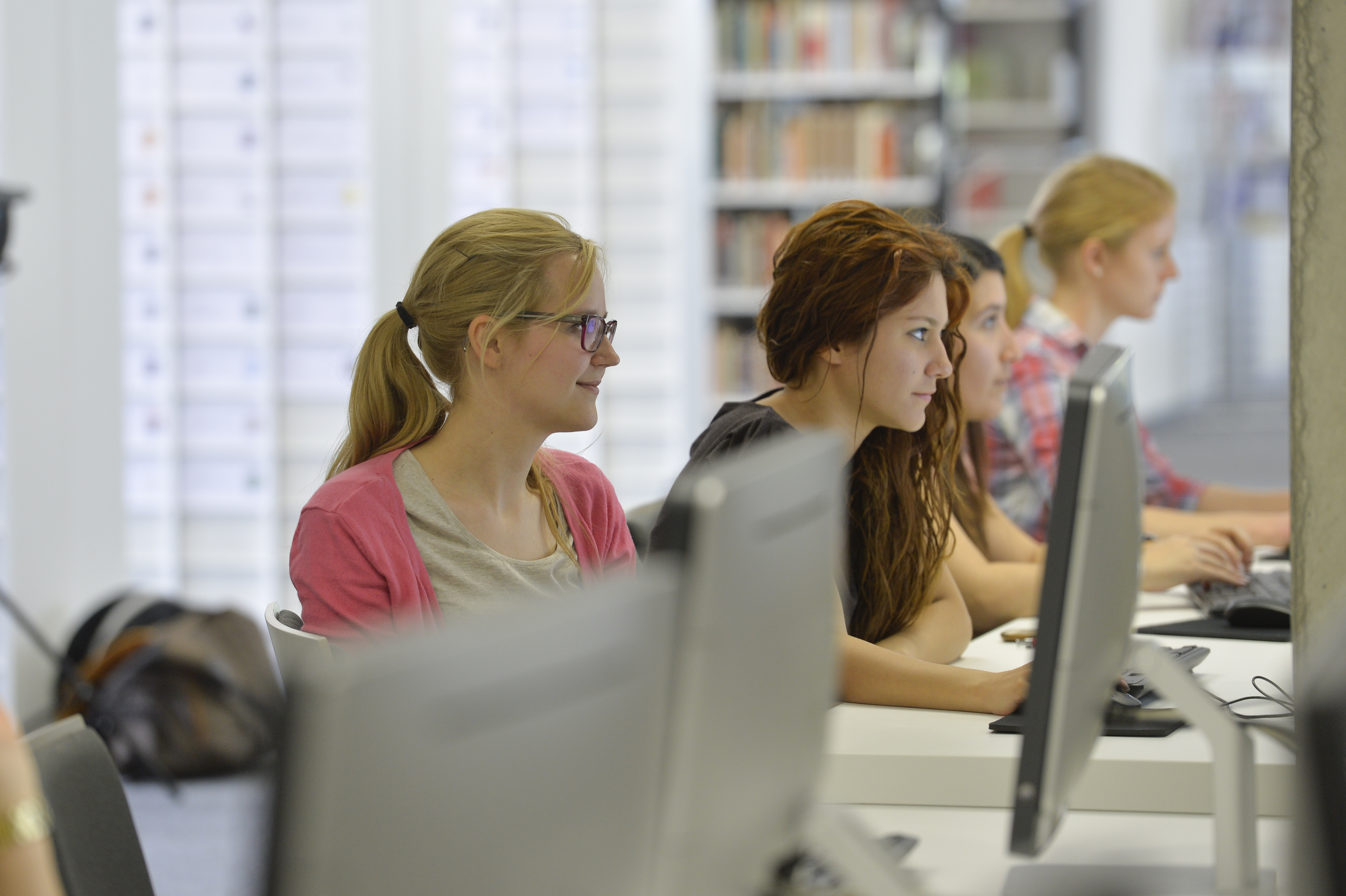 Das Bild zeigt Personen in der Bibliothek, die an Computern sitzen.